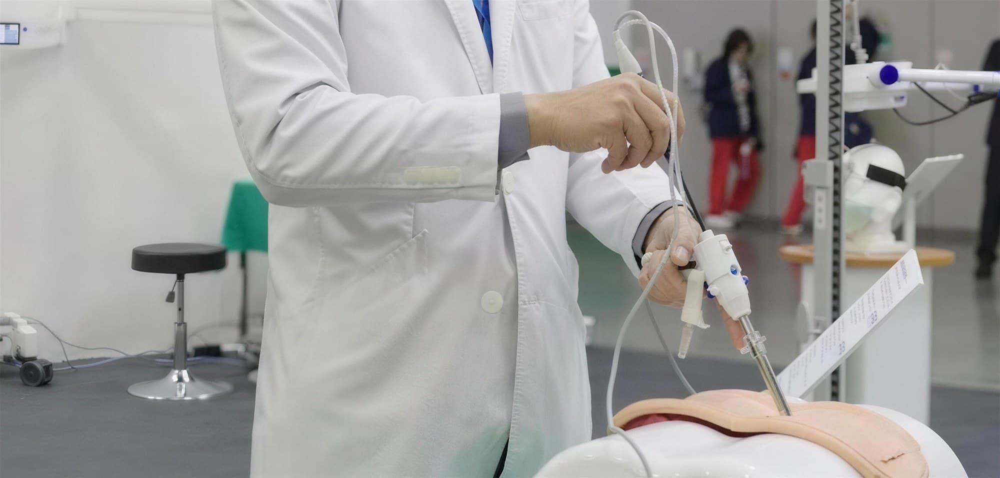 Surgeon in a white coat practicing with the TISE scope on a training phantom in a workshop room